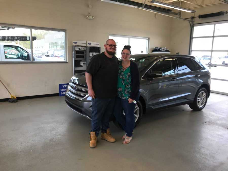 Boyfriend and girlfriend stand inside garage dealership in front of their new car