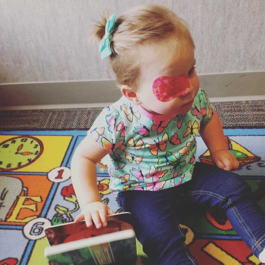 Baby who had Hemorrhagic Stroke sits on floor with pink patch over her left eye