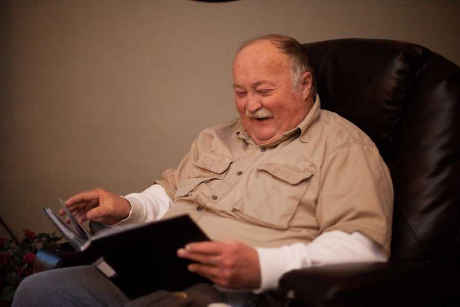 Man laughs as he looks at photo album while sitting in brown leather chair 