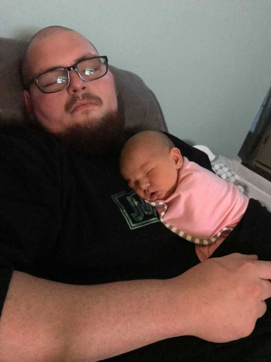 Father lays asleep in chair with baby girl asleep on his chest