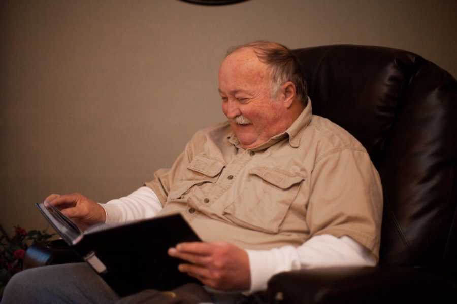 Man smiles as he sits in leather chair looking at photo album