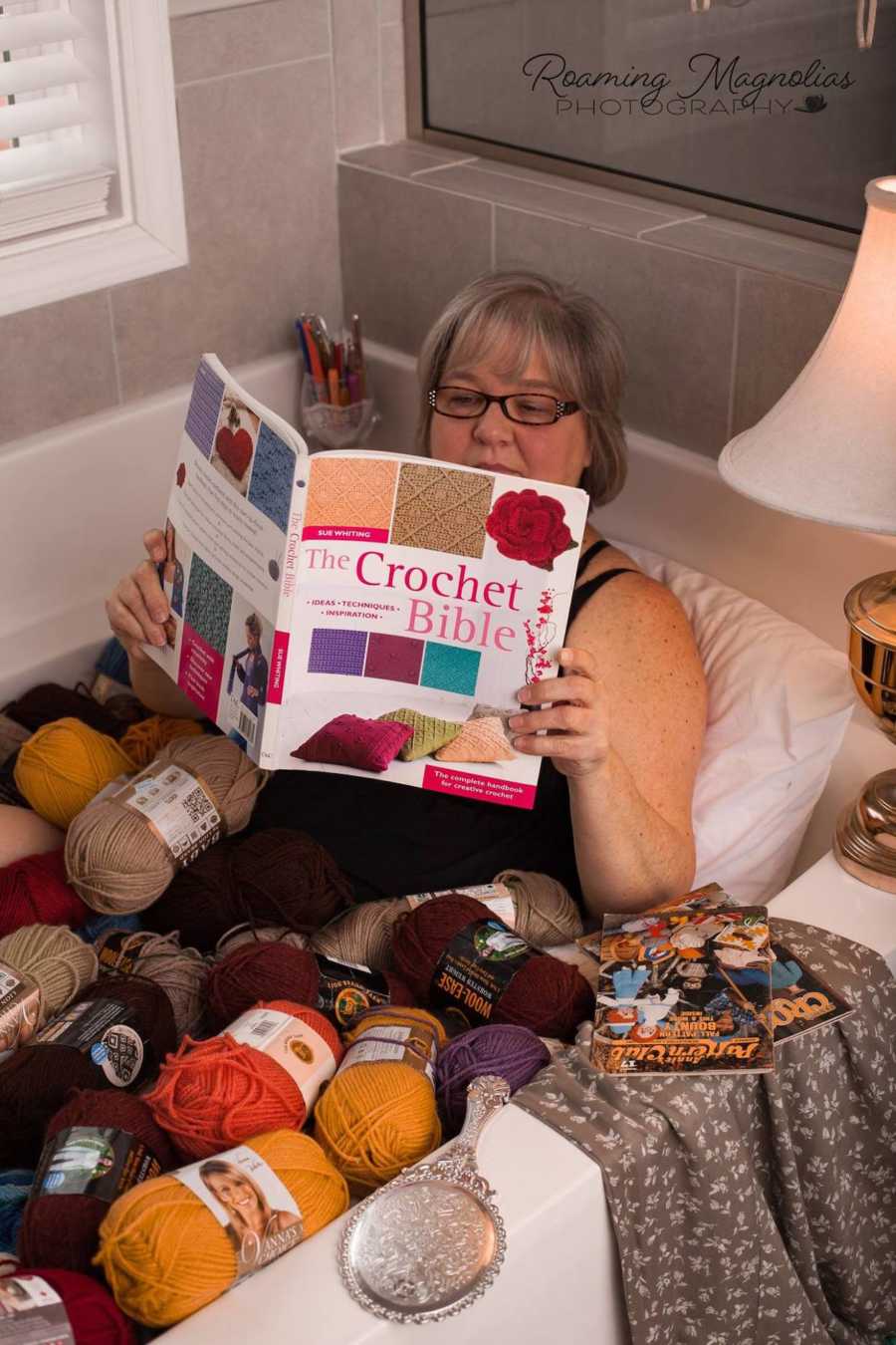 Woman lays in bathtub full of yarn reading magazine called, "The Crochet Bible"