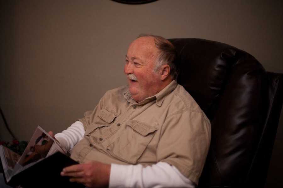 Man laughs as he sits in leather chair flipping though photo album