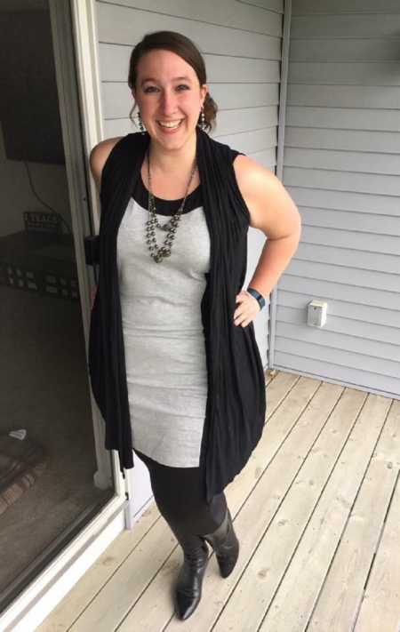 Woman stands on porch of home smiling with hands on her hips