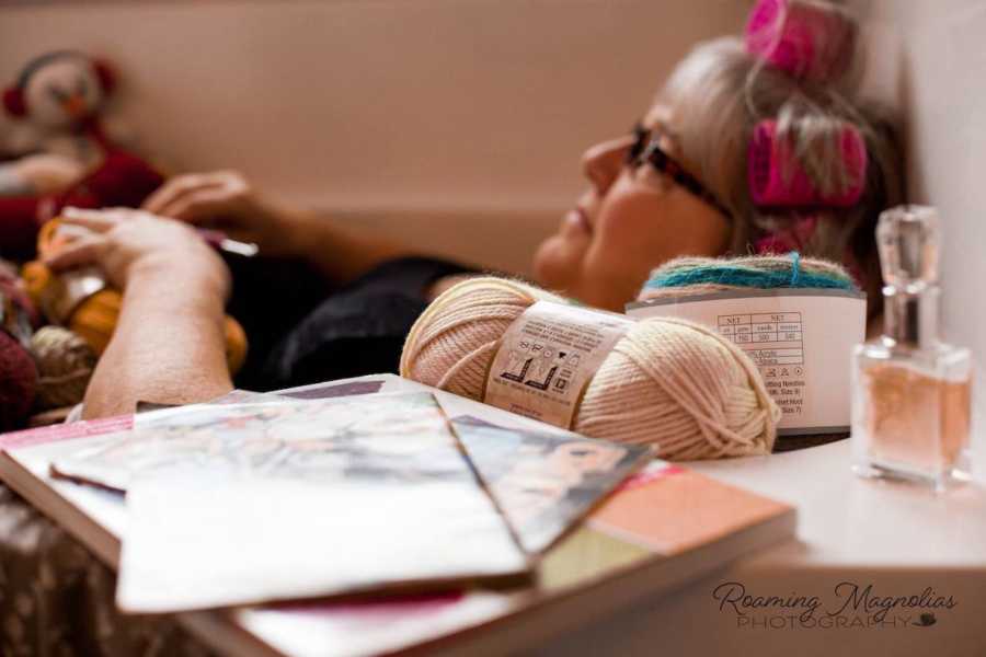 Magazines and a perfume bottle sit on edge of tub where woman lays with yarn covering her