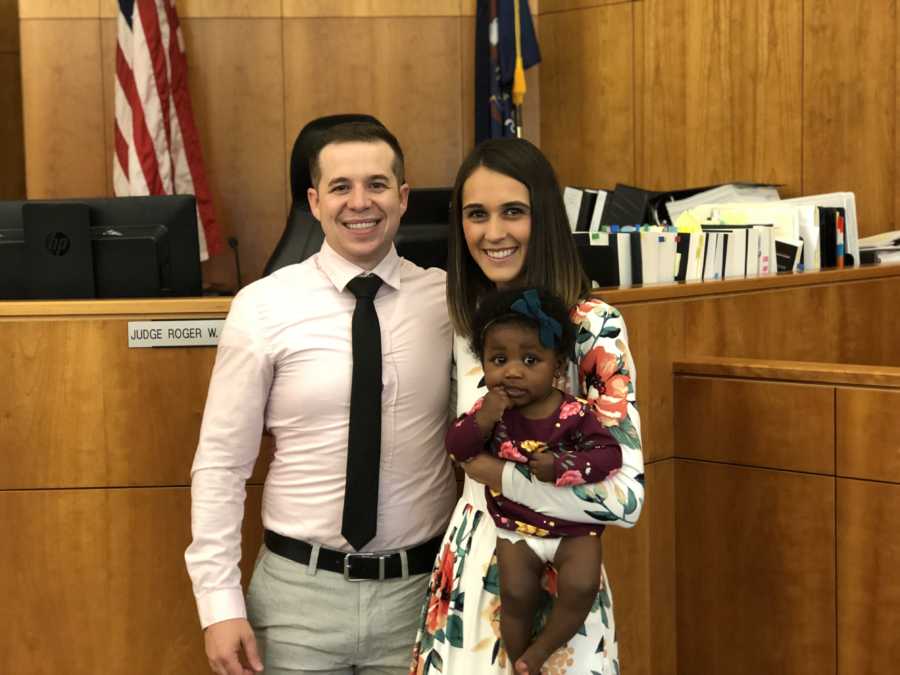 Husband and wife stand at adoption court while wife holds adopted baby girl