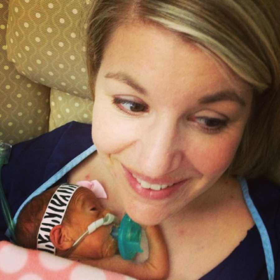 Woman who almost didn't survive child birth sits in chair smiling with newborn laying on her chest