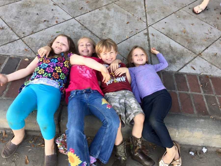 Four children smile as they lay down on side of curb