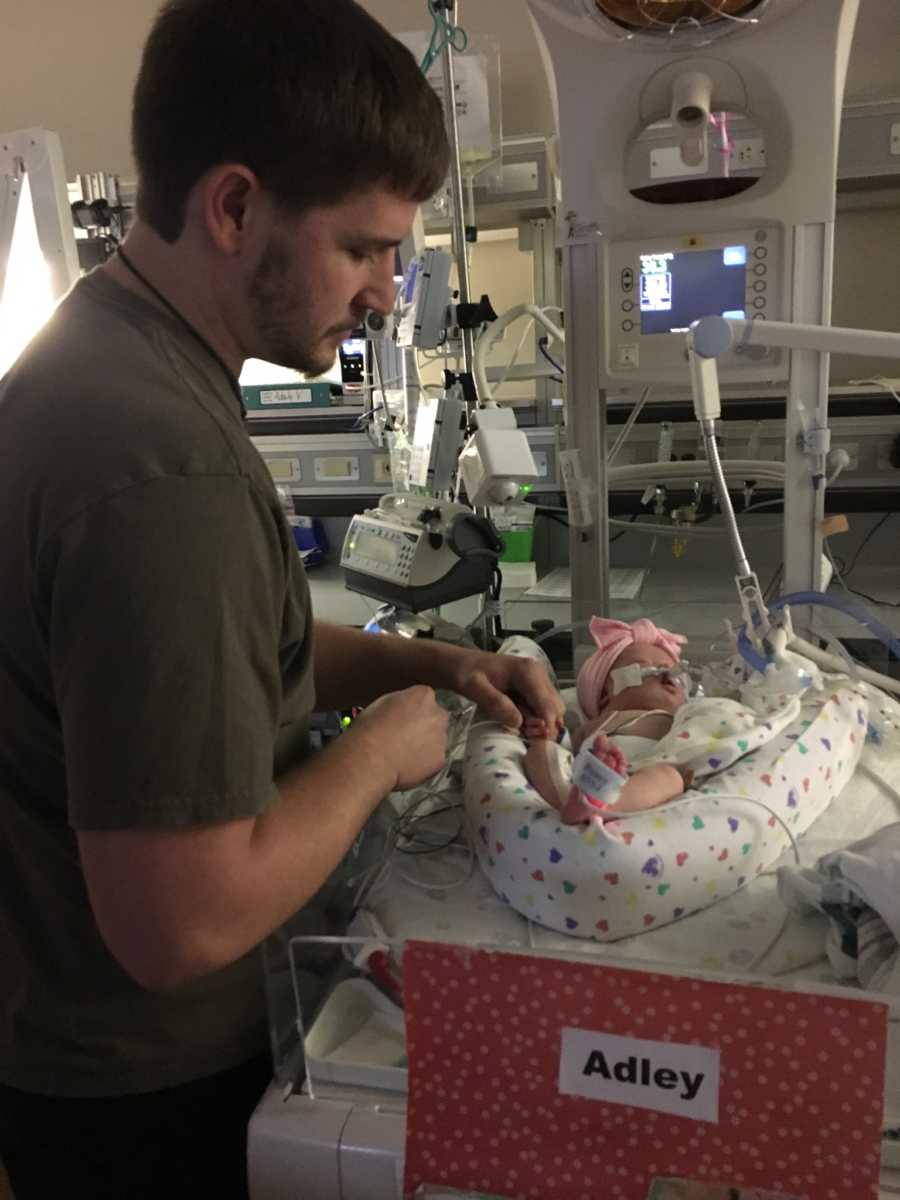 Father stands in NICU holding hand of newborn baby with down syndrome