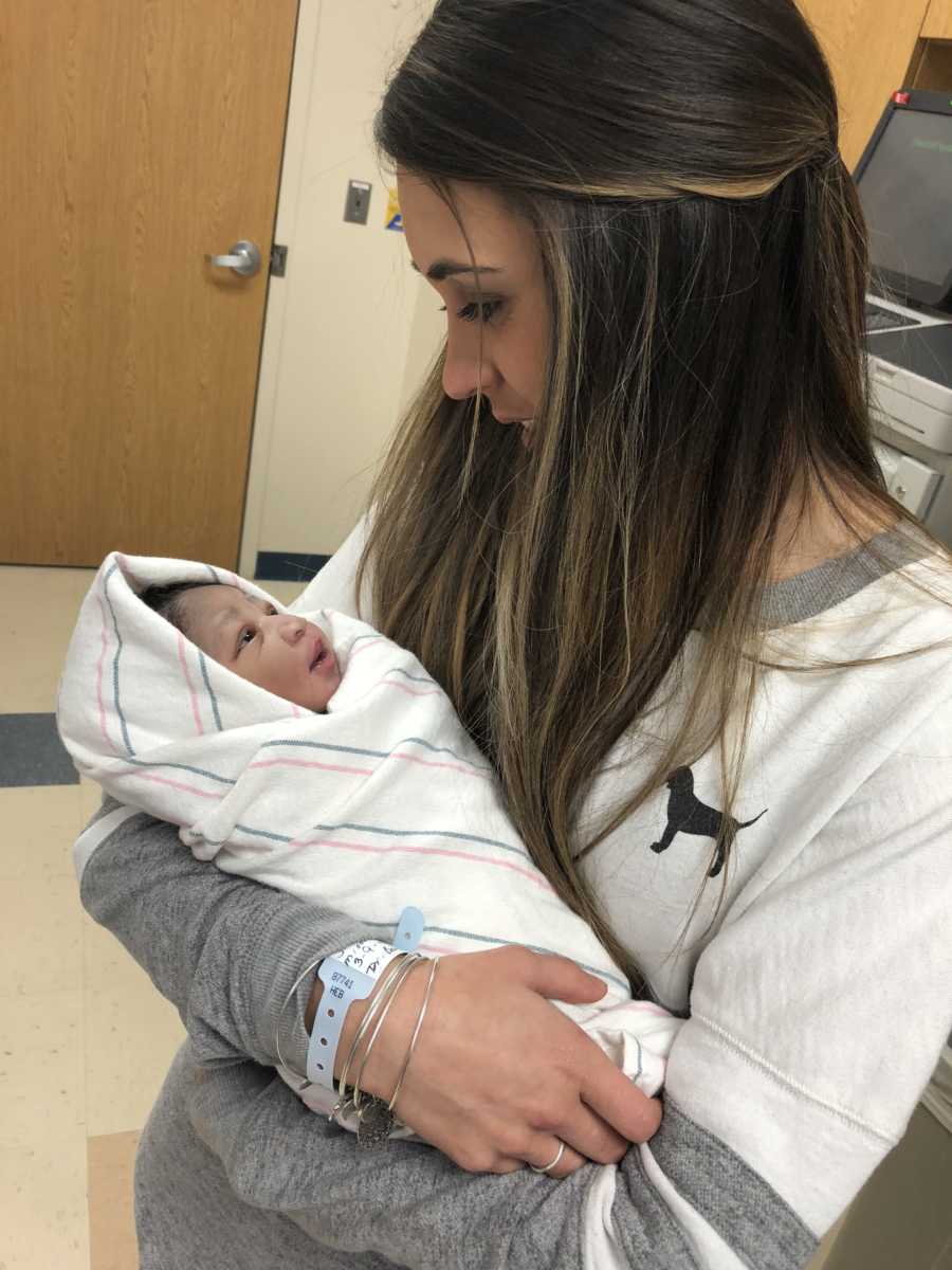 Mother smiles in hospital as she looks down at her adopted newborn