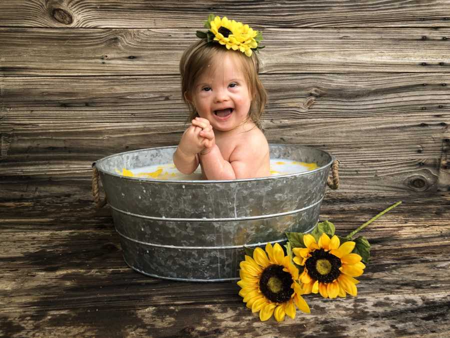 Little girl with down syndrome sits in tin bucket with sunflower on her head and beside bucket