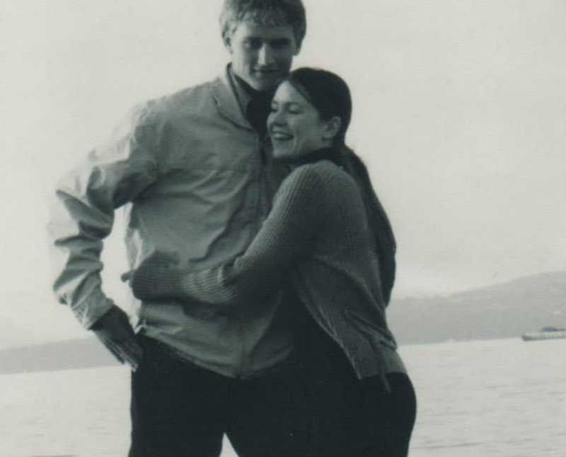 Husband and wife who want to adopt stand smiling with body of water in background