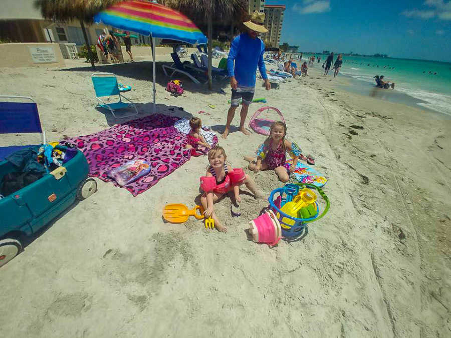 Little girls sit on beach playing with beach toys who will be taken into a foster home