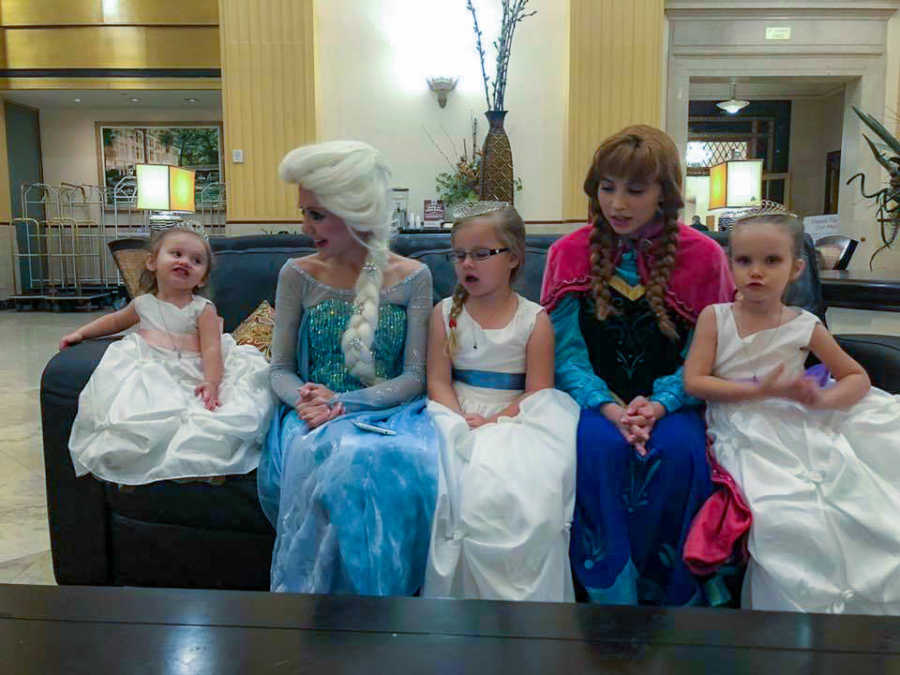 Husband and wife's daughter and two foster daughters sit on couch with Elsa and Anna