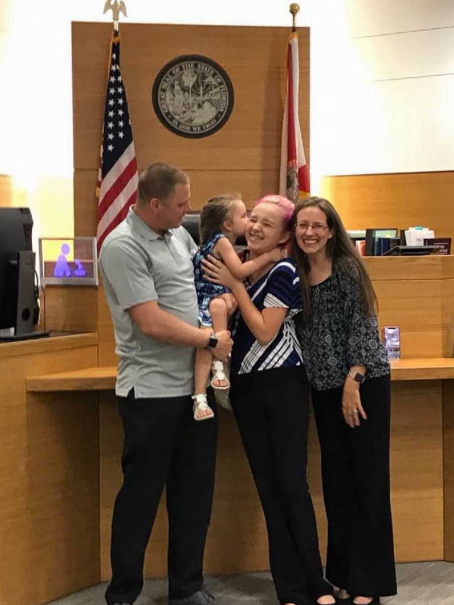 Husband and wife stand at adoption court with their biological teen daughter and young niece they adopted