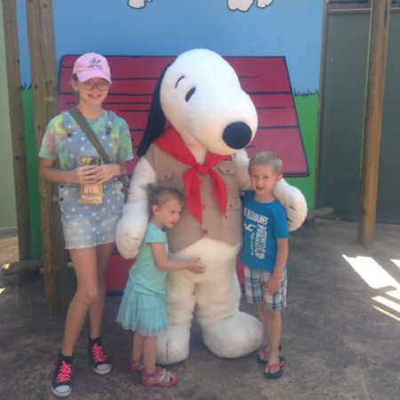 Toddler who was adopted at birth stands hugging snoopy beside her brother and older sister