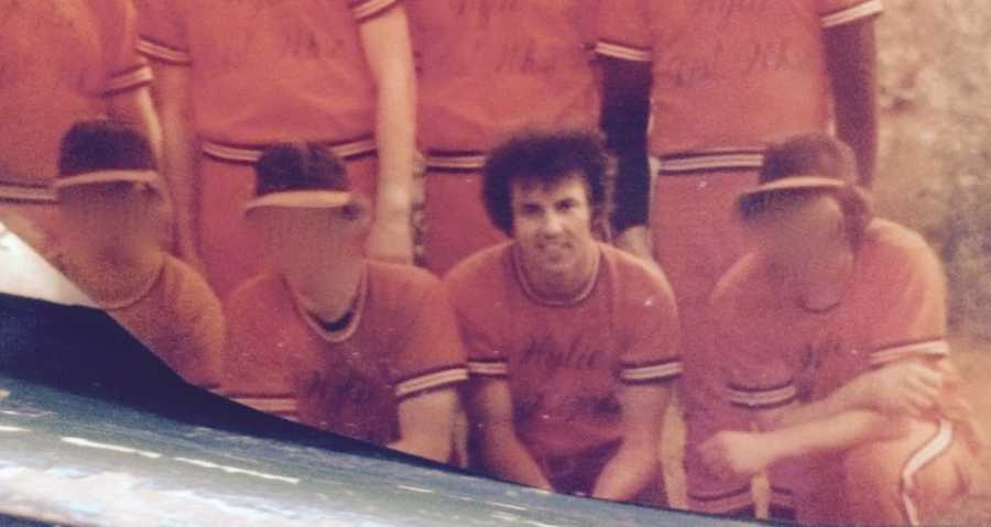 Man kneeling in orange baseball uniform beside others with faces blurred out