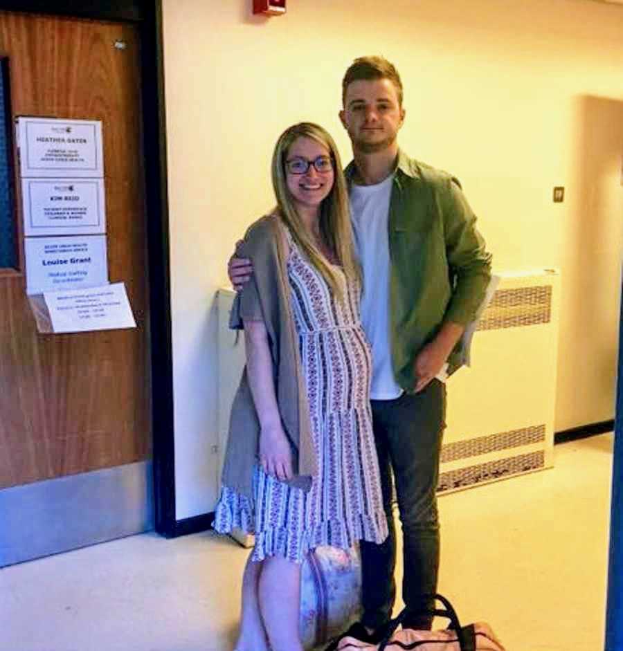 Pregnant woman stands in hospital hallway smiling with husband