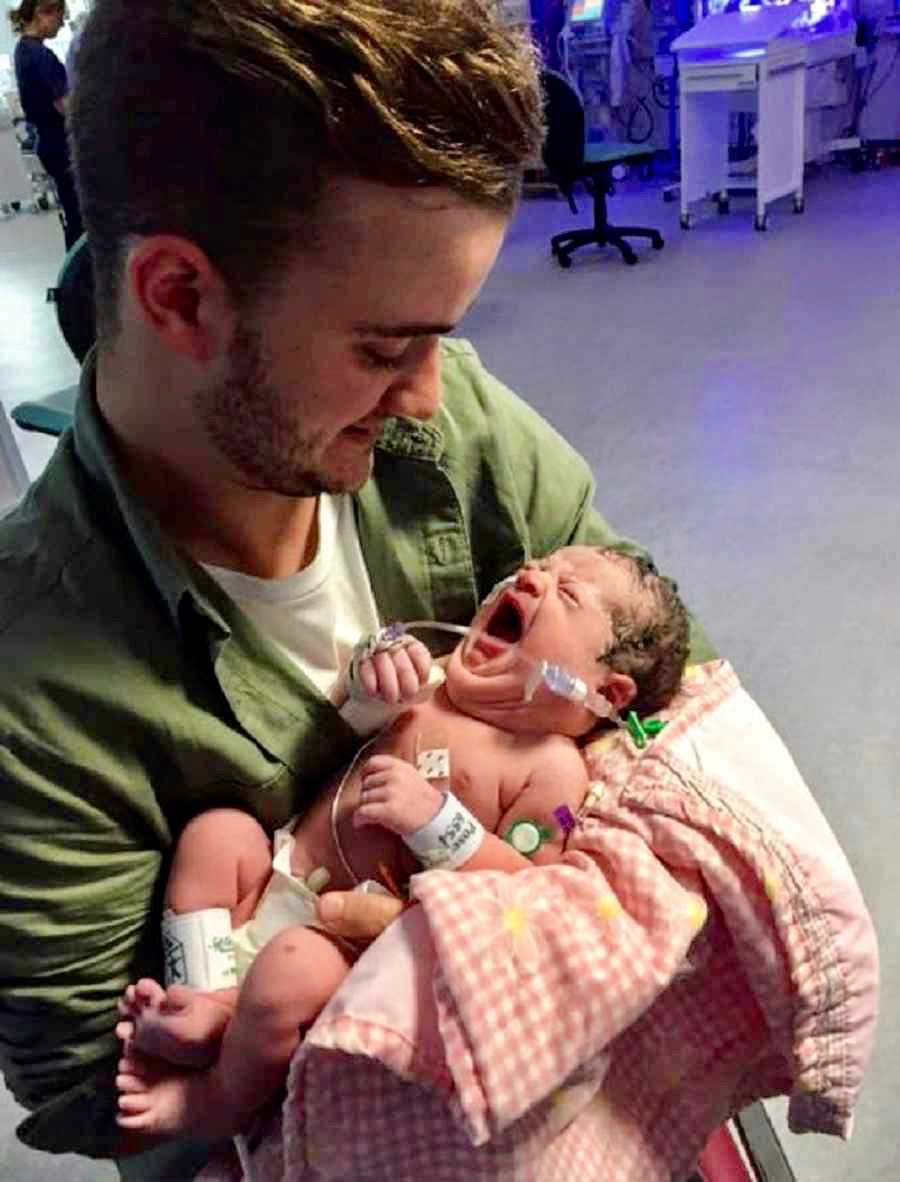 Father smiles as holds newborn with lymphatic malformation in NICU