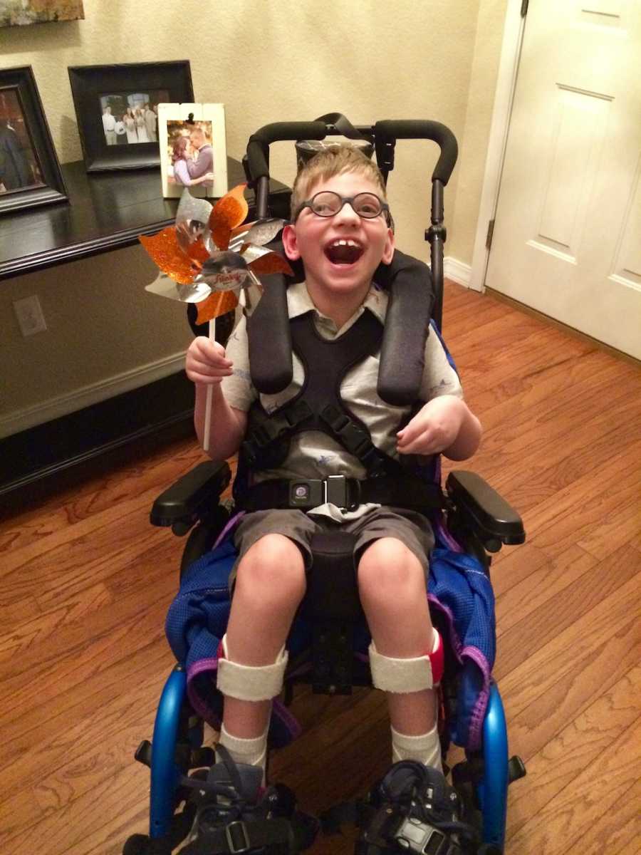 Young boy with shaken baby syndrome sits smiling in wheelchair holding pinwheel