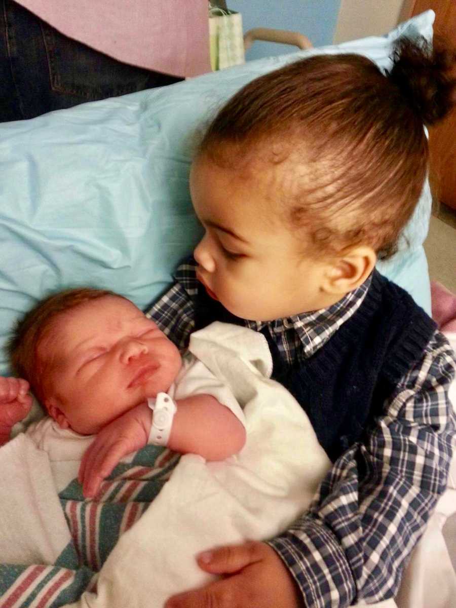 African American little girl holds newborn baby with red hair 