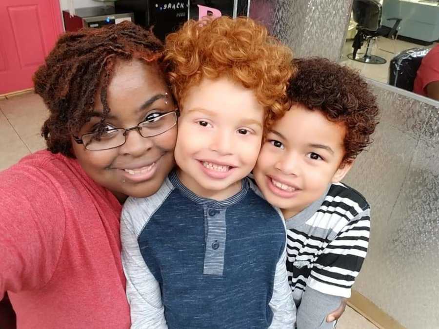 African American mother smiles in selfie with two sons, one of which has red hair