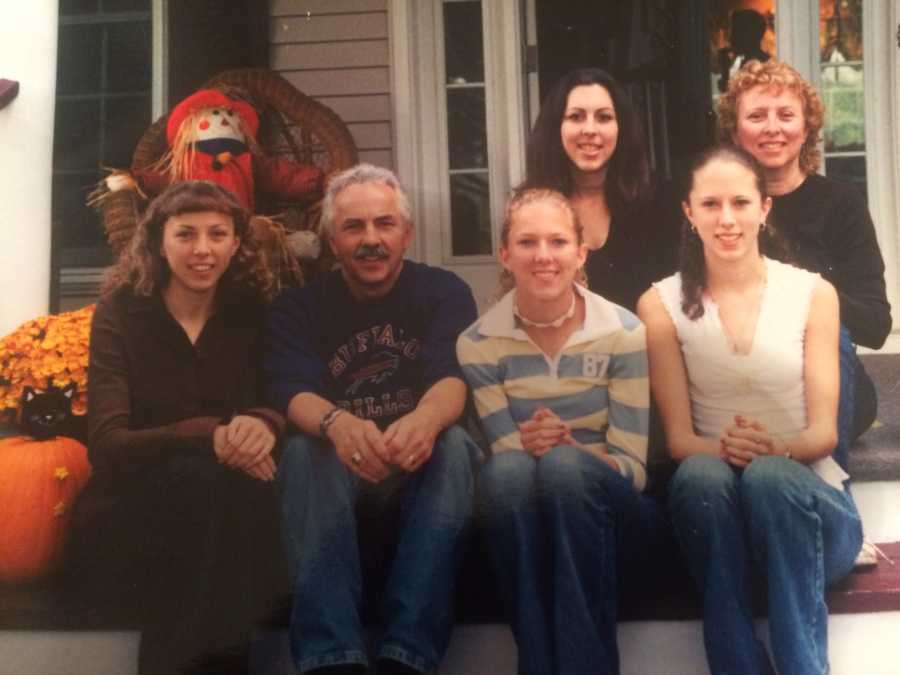 Man who has since passed away sits outside on steps of home decorated for Halloween beside wife and four daughters