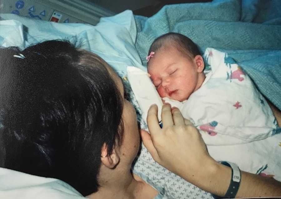 Teen lays in hospital bed looking at newborn swaddled in her arms