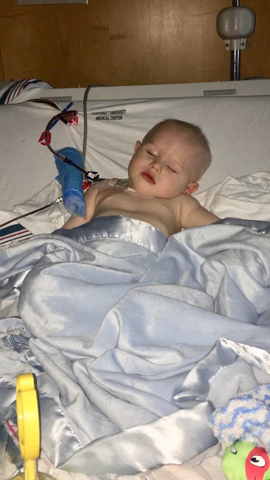 Paralyzed little boy lays asleep in hospital bed covered in blue blanket