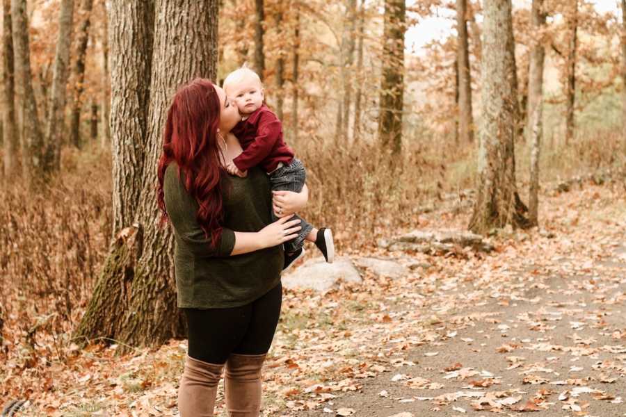 Mother stands on path in forest holding baby with Transverse Myelitis