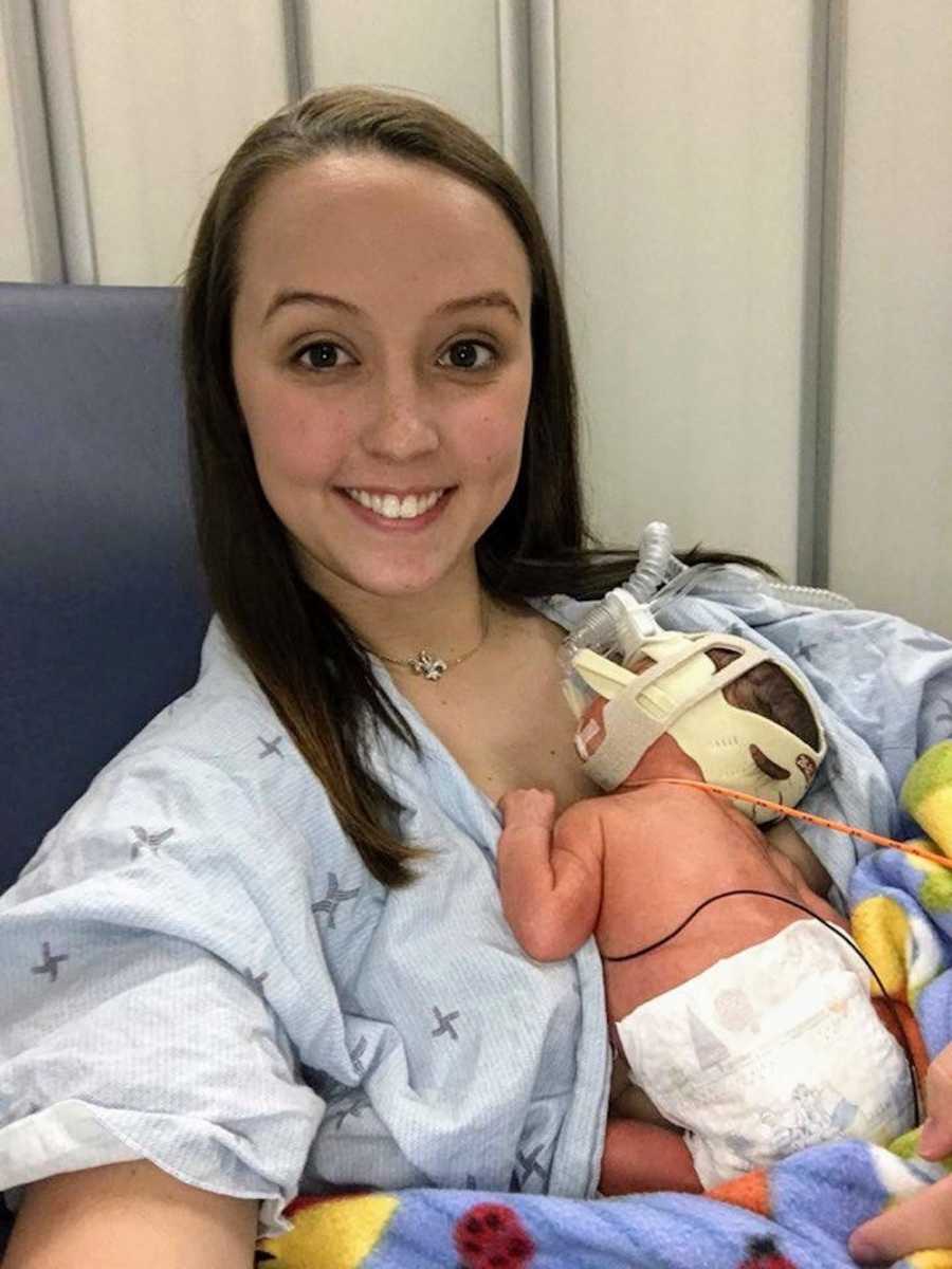 Mother smiles in selfie while sitting in NICU with newborn asleep in her lap
