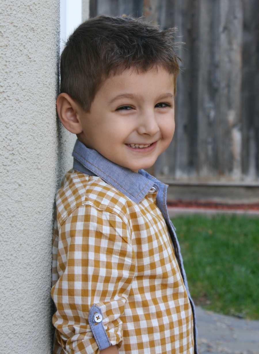 Little boy smiles as he leans his back against wall