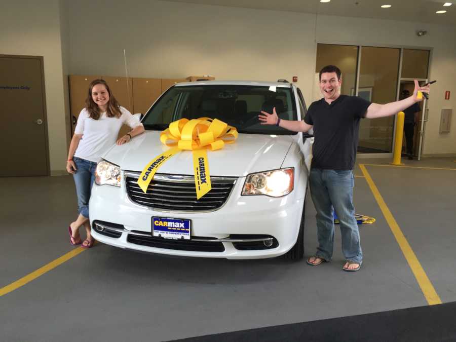 Husband and wife smile beside white mini van they bought from Car Max
