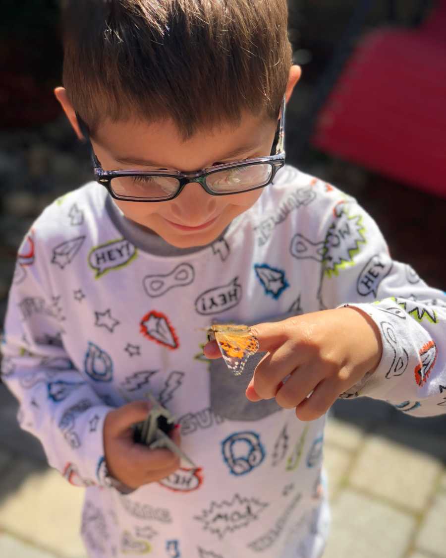 Mother's sweet little boy stands smiling as butterfly sits on his finger