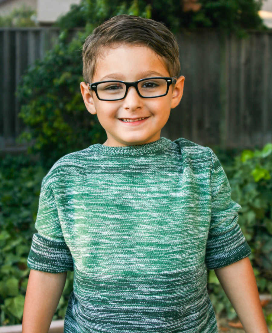 Little boy whose mother fears he will lose his sweetness smiles outside with green sweater on