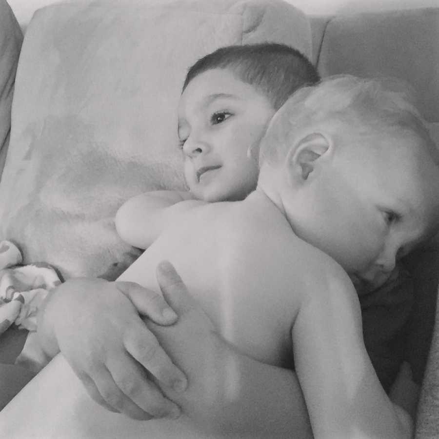 Little boy sits on couch holding baby brother 