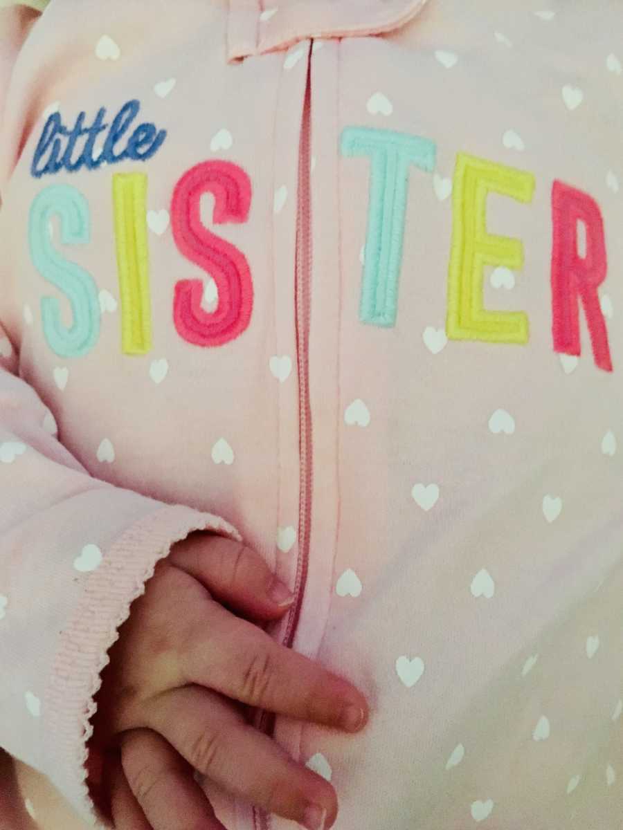 Close up of light big onesie on baby that says, "little sister"