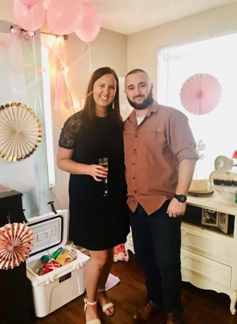 Husband and wife stand smiling at baby shower who will end up losing their baby