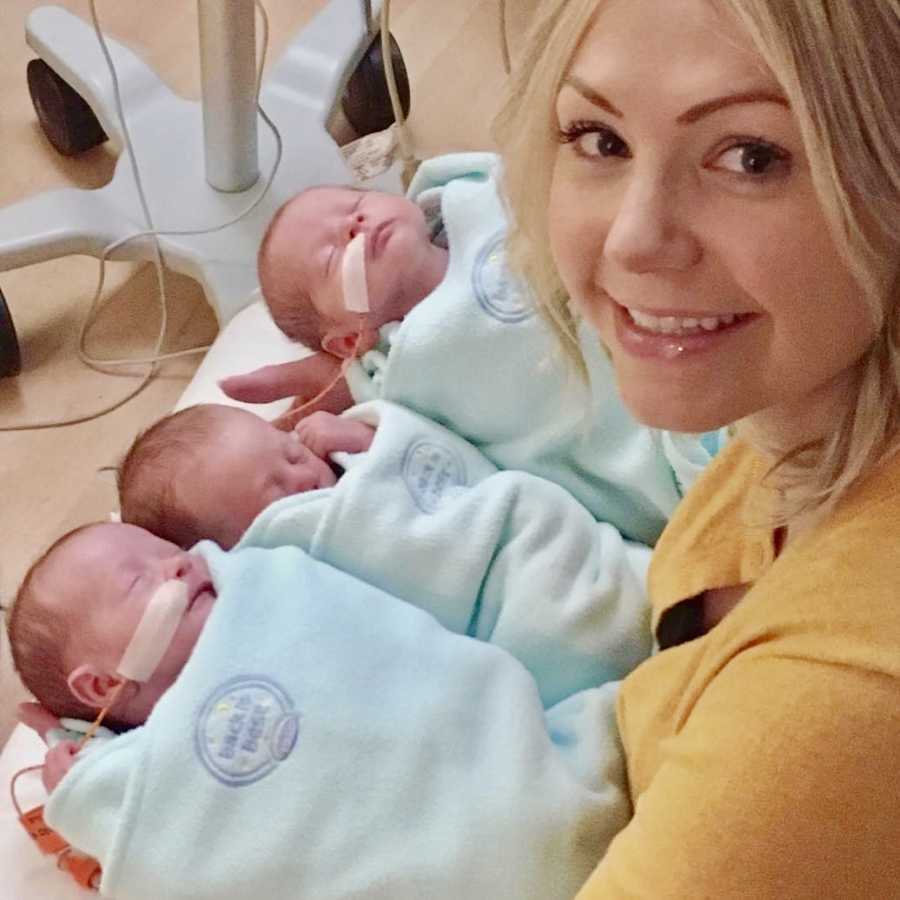 Mother smiles over her shoulder as her three triplets are in her arms