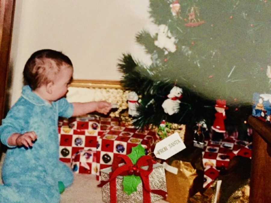 Baby sits beside presents under Christmas tree who has since passed away
