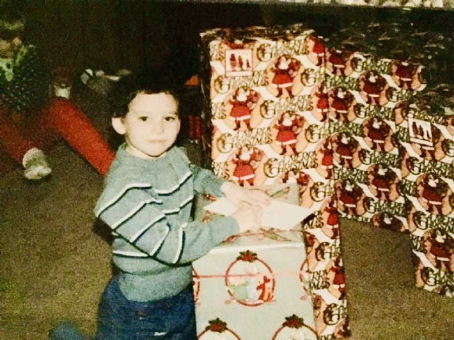 Little boy sits on knees by Christmas presents who has grown up and passed away at young age