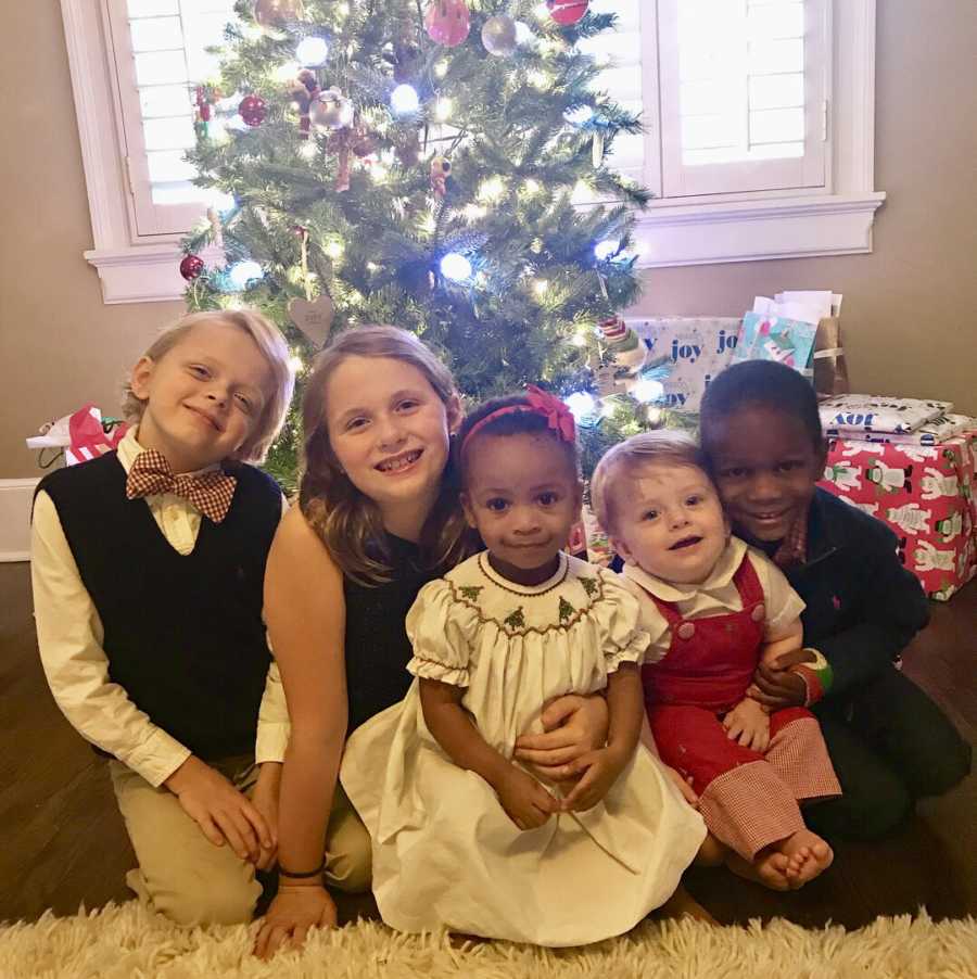 Five siblings sit on floor in front of Christmas tree