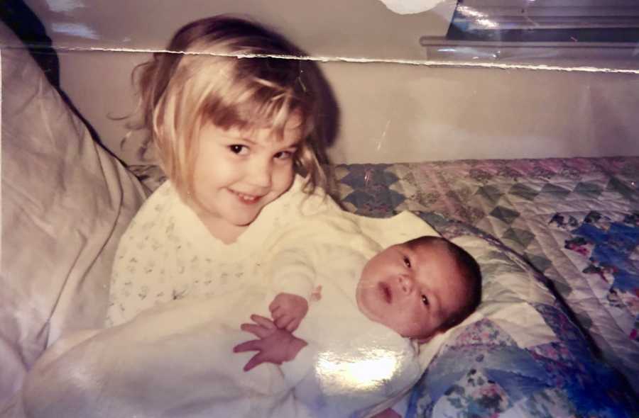 Little girl sitting on bed holding baby sibling