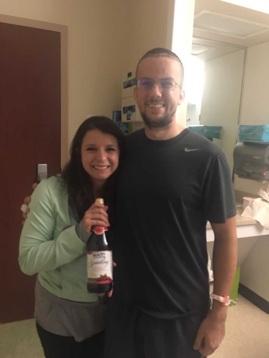 Man who was in car crash stands smiling in hospital beside fiancee who holds bottle of sparkling grape juice