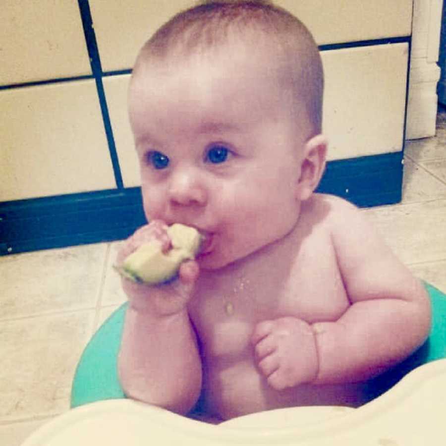 Baby sits on floor of kitchen eating apple