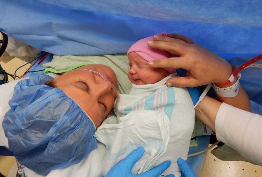 Mother who just had c-section lays in operating room looking at newborn who is being held in front of her