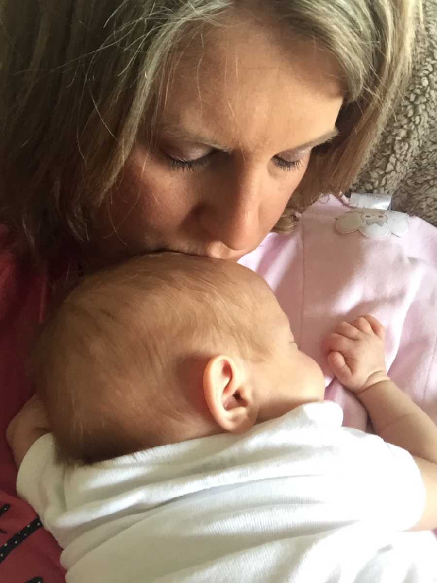 Mother who thought she was infertile closes her eyes while kissing forehead of baby asleep on her lap