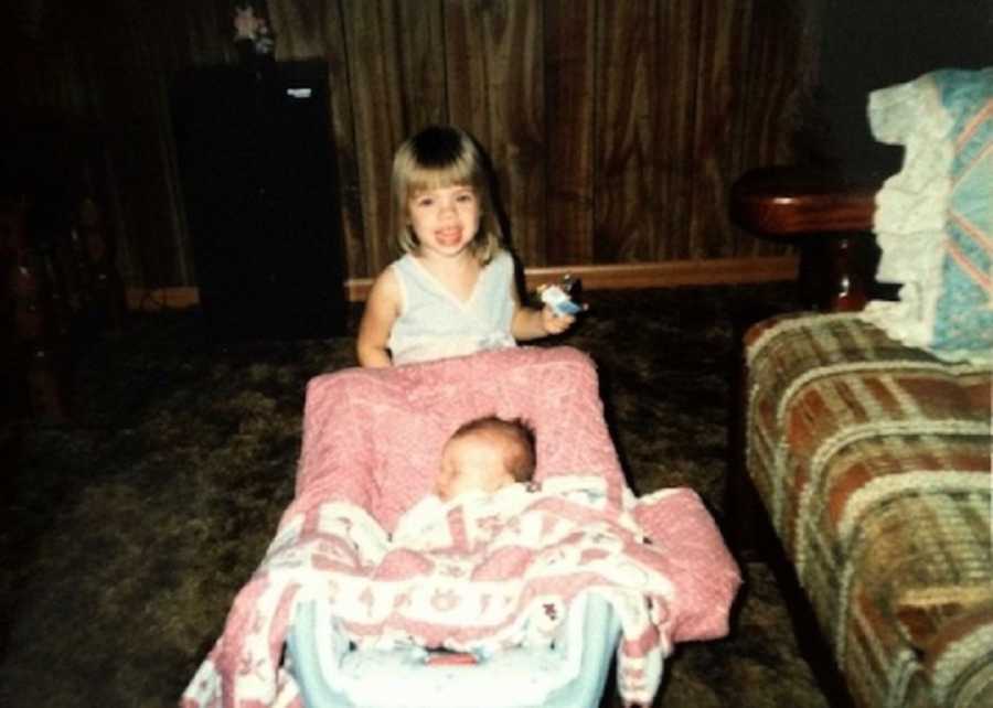 Little girl stands in home over baby who lays asleep 