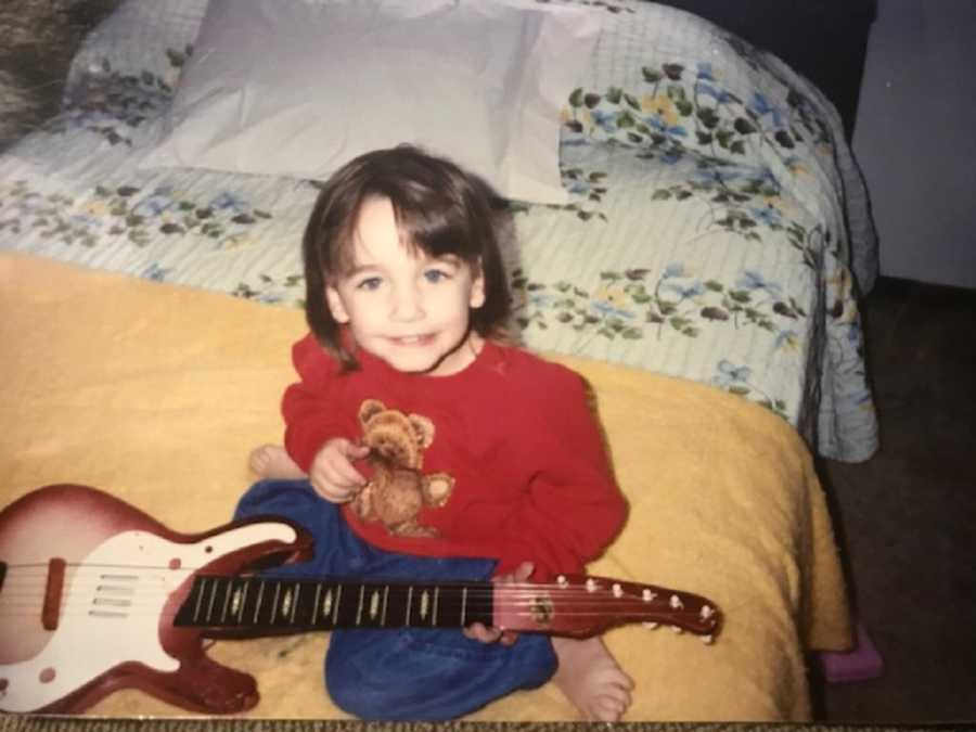 Adopted little girl sits on bed smiling with electric guitar in her lap