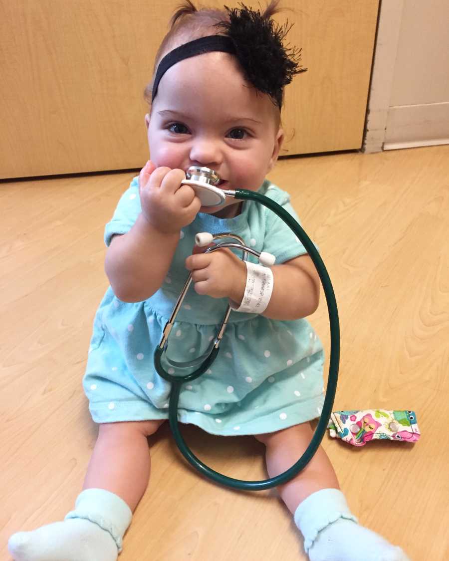 Baby with Celiac Disease and hyperalgesia sits on hospital floor holding stethoscope to her mouth